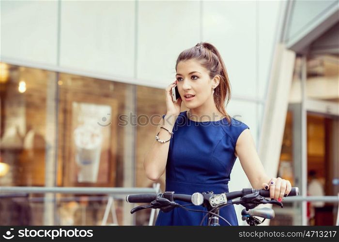 Young woman commuting on bicycle. Young woman in business wear on bicycle and holding mobile phone