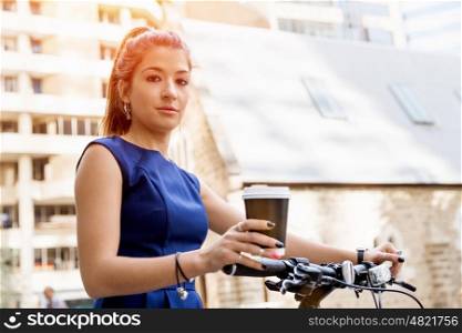 Young woman commuting on bicycle. Young woman in business wear on bicycle with a cup of coffee