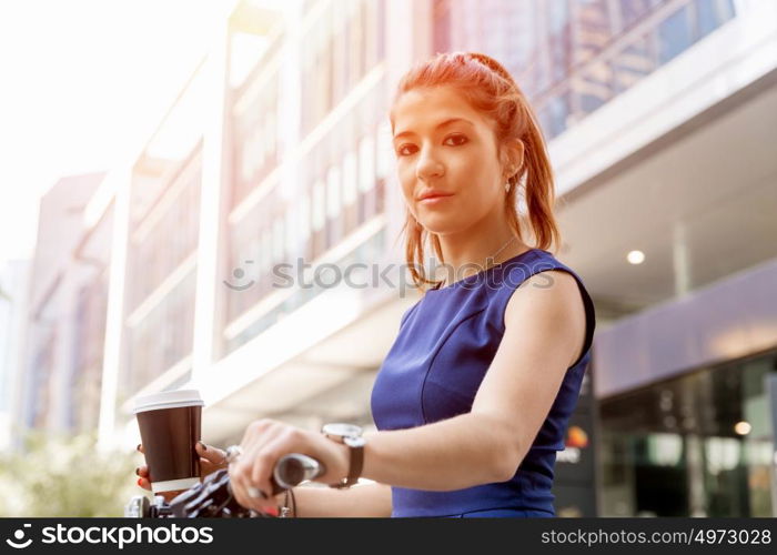 Young woman commuting on bicycle. Young woman in business wear on bicycle with a cup of coffee