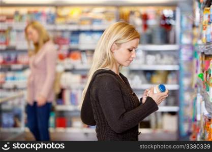 Young woman comparing products in the supermarket with people in the background