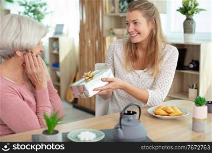 young woman congratulating her senior mother with gift box
