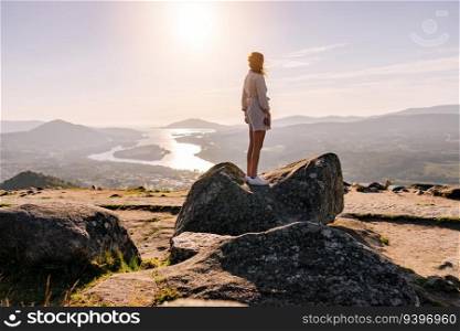 Young woman contemplating the landscape from the top of a rock, with a river and mountains