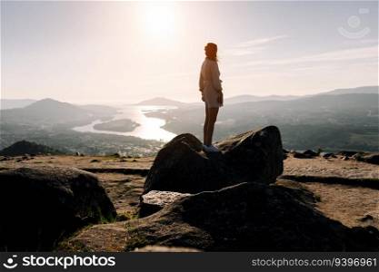 Young woman contemplating the landscape from the top of a rock, with a river and mountains