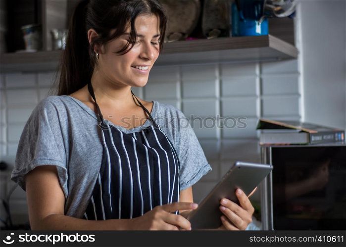 Young Woman cooking and following recipe on Digital tablet in the kitchen at home. Healthy Food.
