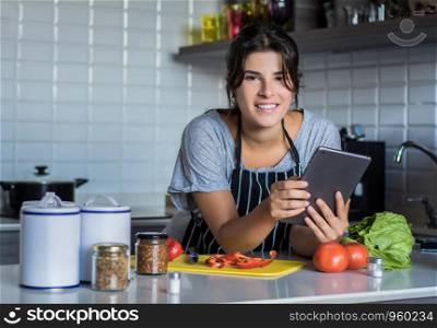 Young Woman cooking and following recipe on Digital tablet in the kitchen at home. Healthy Food.