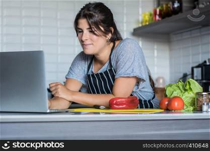 Young Woman cooking and following recipe on laptop pc in the kitchen at home. Healthy Food.