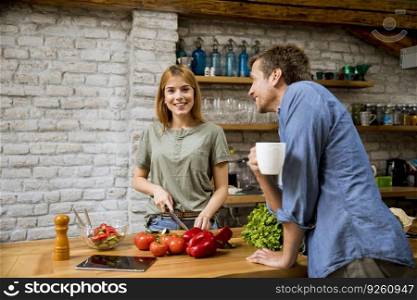 Young  woman cooking while man drinking coffee  in the rustic kitchen