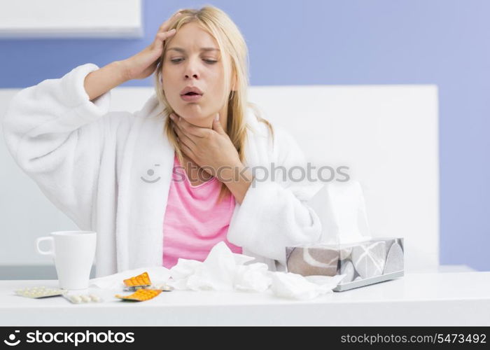 Young woman coughing while suffering from headache and cold in kitchen