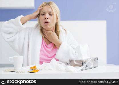 Young woman coughing while suffering from headache and cold in kitchen