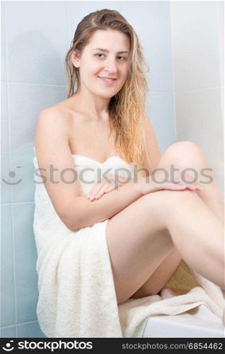 Young woman covered in white bath towel sitting at bathroom