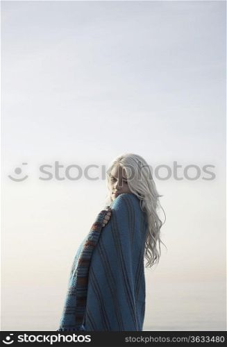 Young woman covered with blanket against sky