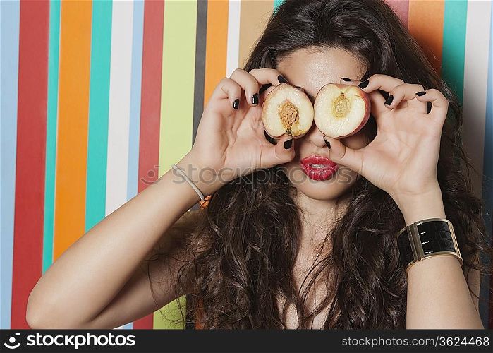 Young woman covering her eyes with peach against striped background