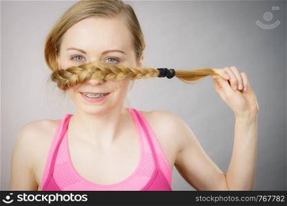 Young woman covering her mouth with blonde hair braid. Haircare and hairstyling concept.. Woman covering her mouth with blonde braid