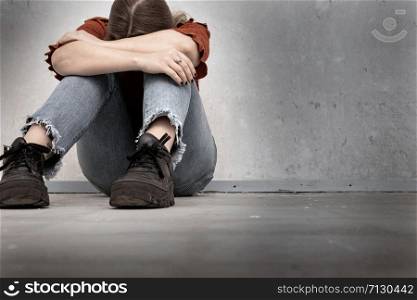 Young woman cries and sitting near a empty wall, lonely sad and depressed girl holding her head down closeup. Young woman cries and sitting near a empty wall, lonely sad and depressed girl holding her head down