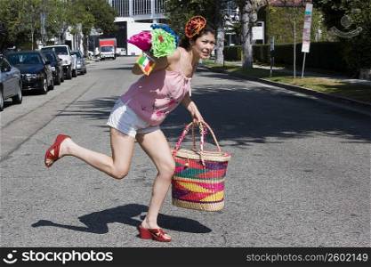 Young woman crossing the street carrying colorful bag and flowers