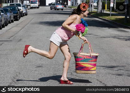 Young woman crossing the street carrying colorful bag and flowers
