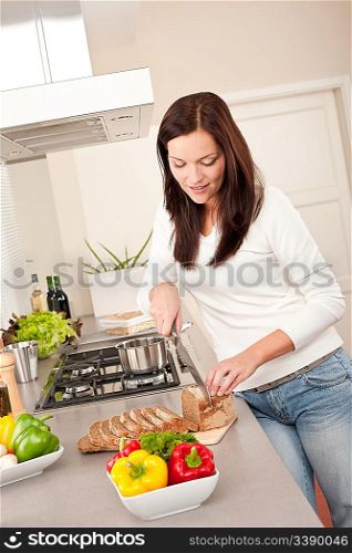 Young woman cutting bread in modern kitchen