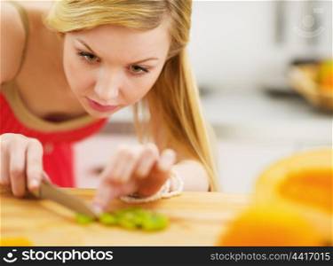 Young woman cutting salad in kitchen