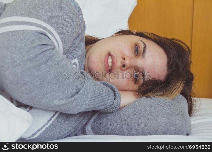 Young woman daydreaming while lying on bed under the blanket.