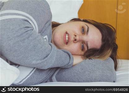 Young woman daydreaming while lying on bed under the blanket.