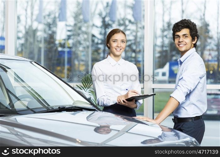 Young woman dealer in auto salon presenting car to customer. This car is perfect for you