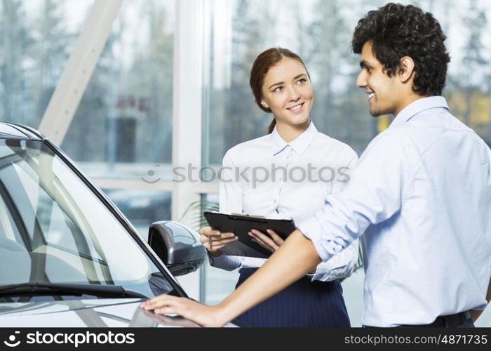 Young woman dealer in auto salon presenting car to customer. This car is perfect for you