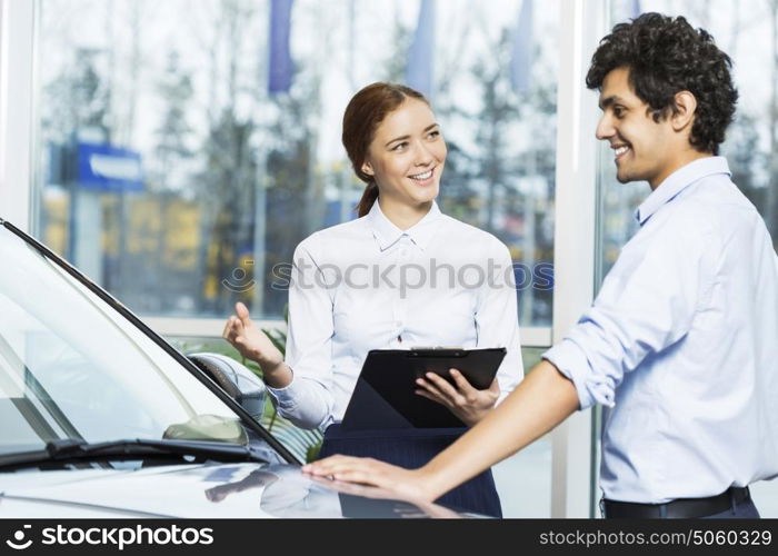 Young woman dealer in auto salon presenting car to customer. This car is perfect for you