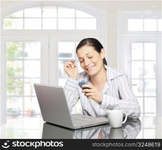 Young woman dials on cellphone over a laptop computer. There is morning at home in a light and clean living room dominated by white and soft tones.