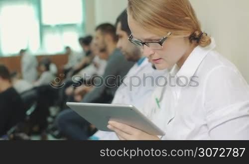 Young woman doctor or student using tablet computer to take notes during medical conference, symposium or lecture