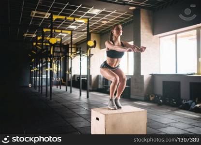 Young woman doing box jump exercise in fitness club. Attractive female athlete workout in gym. Woman doing box jump exercise in fitness club
