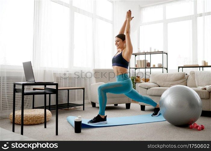 Young woman doing exercise at home, online pilates training at the laptop. Female person in sportswear, internet sport workout, room interior on background. Woman doing exercise, online pilates training