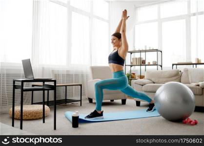 Young woman doing exercise at home, online pilates training at the laptop. Female person in sportswear, internet sport workout, room interior on background. Woman doing exercise, online pilates training