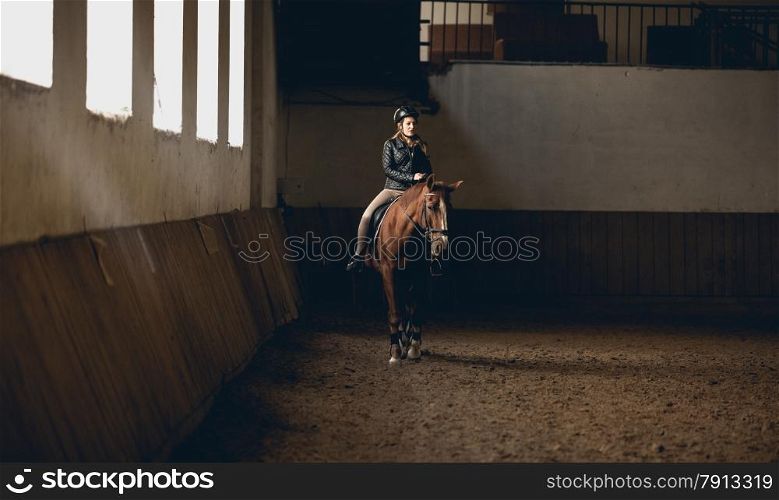 Young woman doing horseback riding in indoor manege