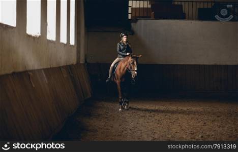 Young woman doing horseback riding in indoor manege