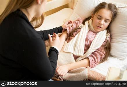 Young woman doing injection to girl lying in bed