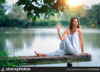 Young woman doing seated spinal twist by the lake. Ardha Matsyendrasana