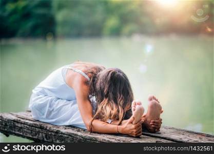 Young woman doing seated spinal twist by the lake. Seated forward bend yoga pose. Paschimottanasana.