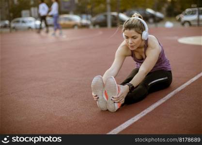 Young woman doing some warm up exercises and streching legs at the court at outdoor