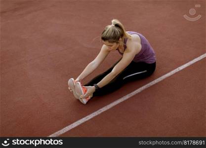Young woman doing some warm up exercises and streching legs at the court at outdoor