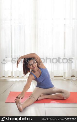 Young woman doing stretching exercise on mat at home