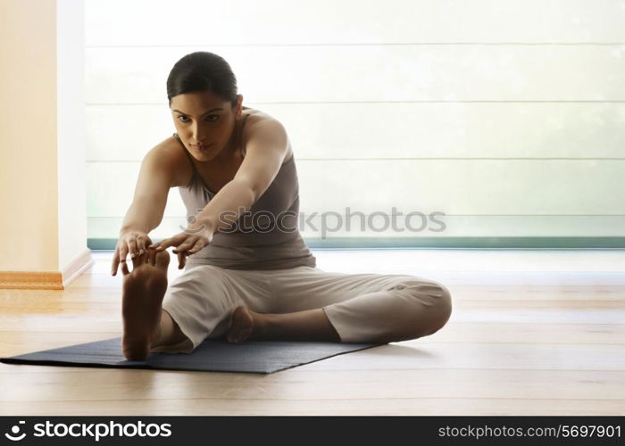 Young woman doing stretching exercise on yoga mat