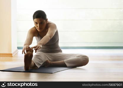 Young woman doing stretching exercise on yoga mat