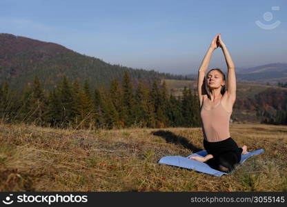 Young woman doing stretching exercises on nature in mountains. Sports girl practicing yoga pose in leggings. beautiful forest landscape