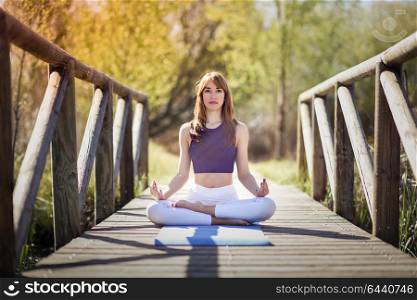 Young woman doing yoga in nature. Female wearing sport clothes in lotus figure.