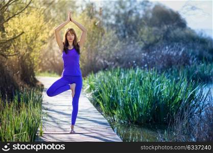 Young woman doing yoga in nature. Female wearing sport clothes in tree figure on a wooden road.