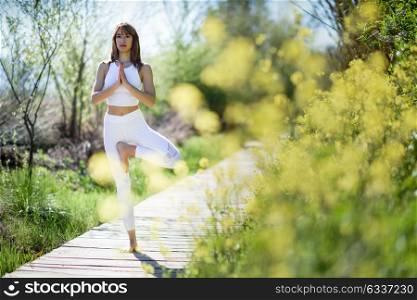 Young woman doing yoga in nature. Female wearing sport clothes in tree figure.