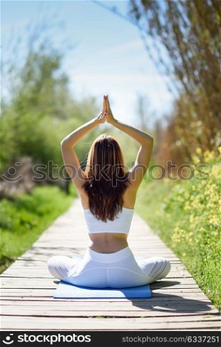 Young woman doing yoga in nature. Female wearing white sport clothes in lotus figure.