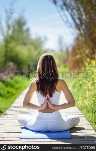Young woman doing yoga in nature. Female wearing white sport clothes in lotus figure.
