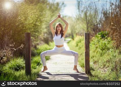Young woman doing yoga in nature. Female wearing white sport clothes on a wooden road.
