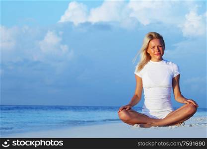 Young woman doing yoga lotus exercise outdoors on sea beach. Yoga woman on sea coast